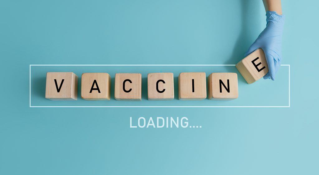 Healthcare professional holding wooden blocks spelling "VACCINE" against blue background.
